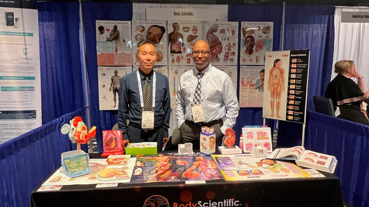 Lik Kwong and Marcelo Oliver standing at their stand in front of medical education items.